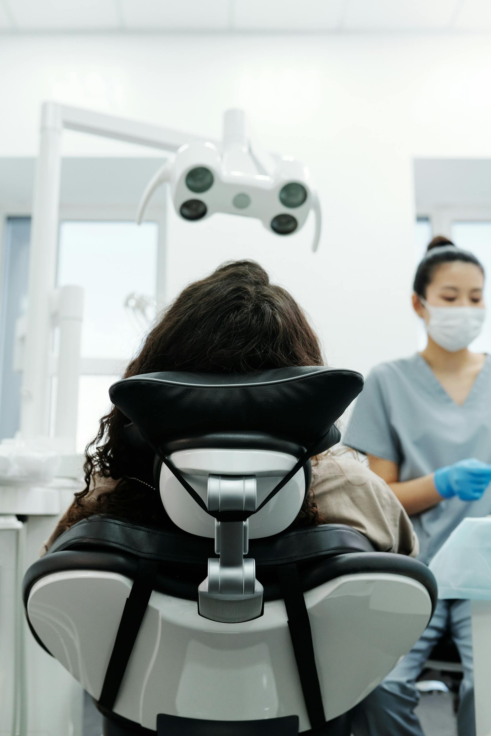 Patient sitting in a modern dental chair, attended by a dentist in a clinic.