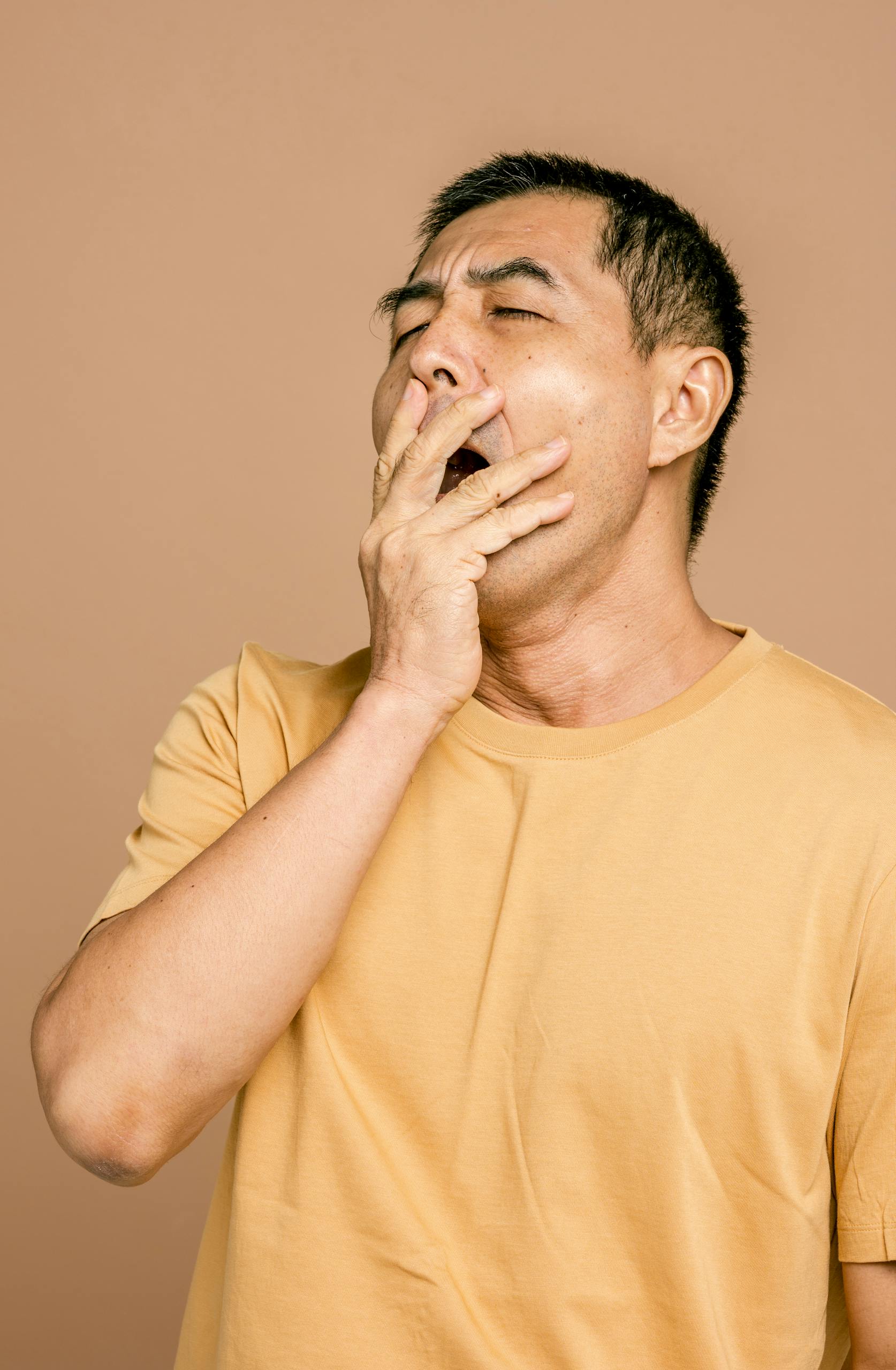 Portrait of a tired man with eyes closed yawning, covering mouth with hand.