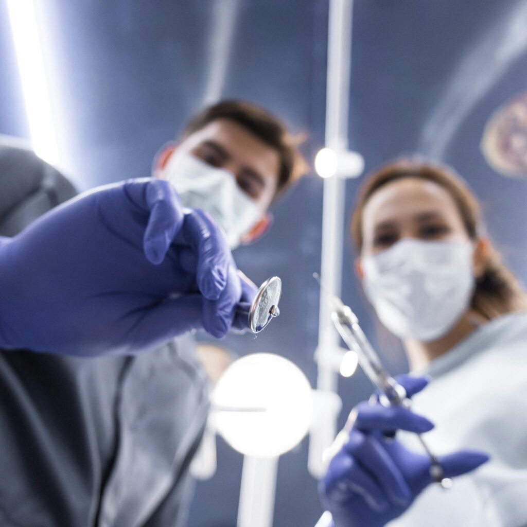 Two dentists in masks and gloves holding dental tools from a low angle view.