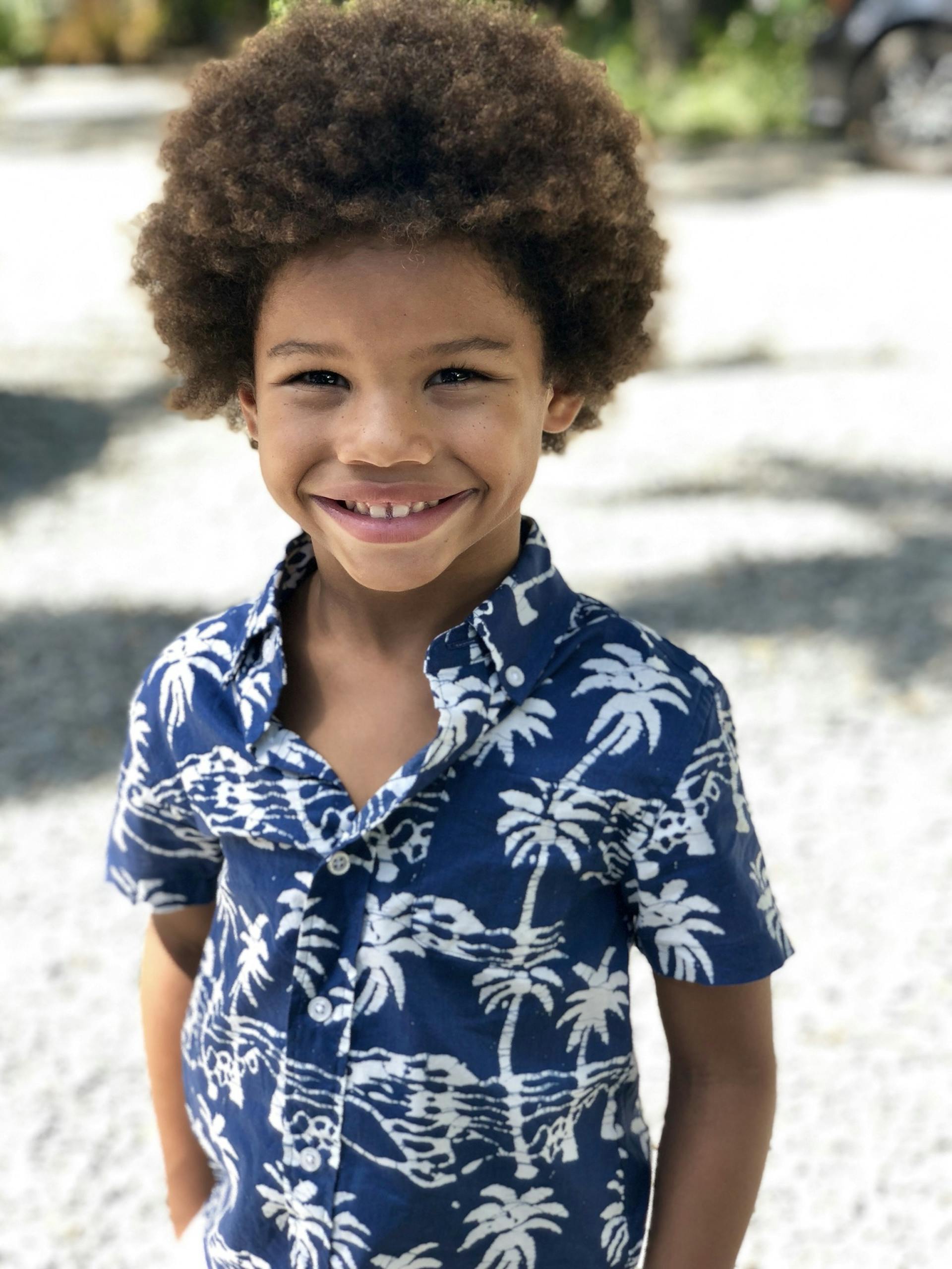 Adorable young boy with an afro smiling brightly outdoors on a sunny day.