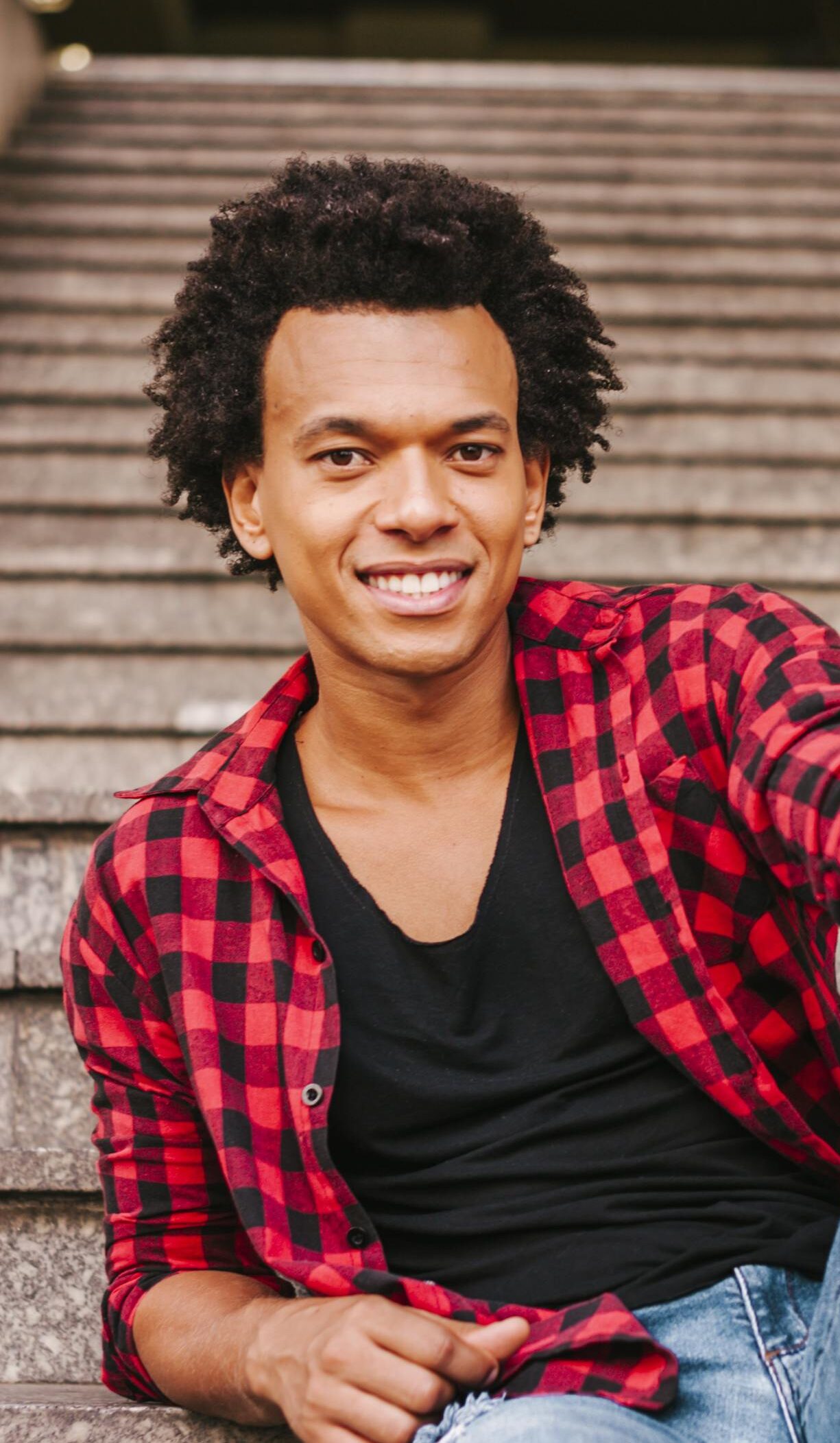 Handsome man sitting on urban stairs, smiling, in casual wear.