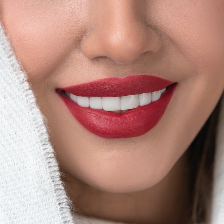 Close-up of a smiling woman with vibrant red lips and perfect teeth.