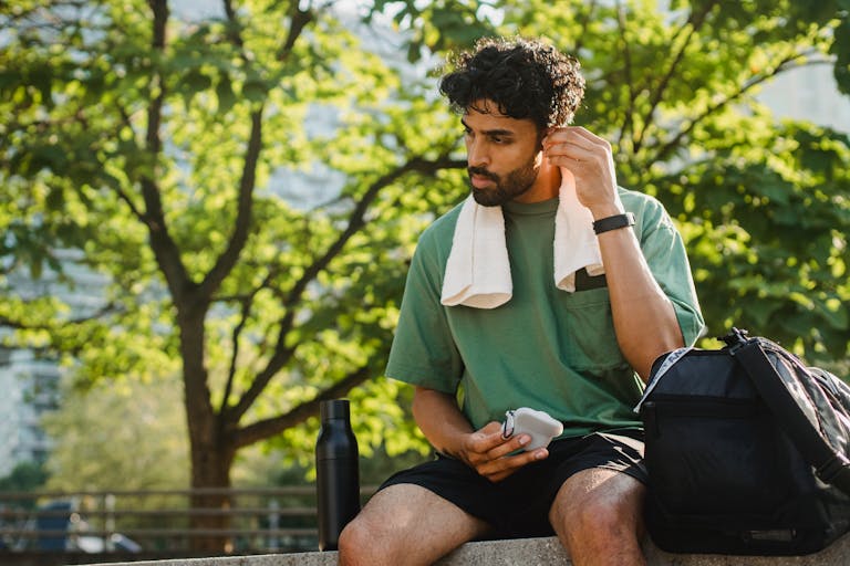 A man in a green shirt relaxes in a sunny park with a towel and water bottle. Perfect for lifestyle imagery.